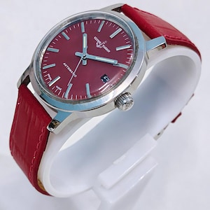 May include: A stainless steel wristwatch with a burgundy dial and a red leather strap. The watch face features silver-tone hands and markers, with the text "ULYSSE NARDIN" and "AUTOMATIC". The watch is displayed on a white stand.