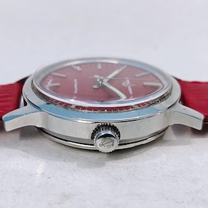 May include: A silver wristwatch with a red face and a red leather band. The watch has a round face with silver hands and markers. The band is a bright red color.