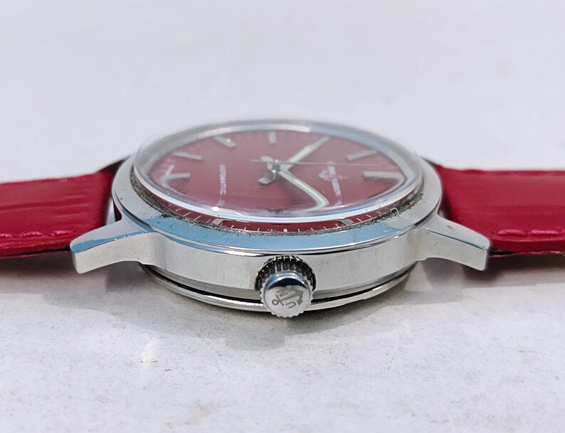 May include: A silver wristwatch with a red face and a red leather band. The watch has a round face with silver hands and markers. The band is a bright red color.