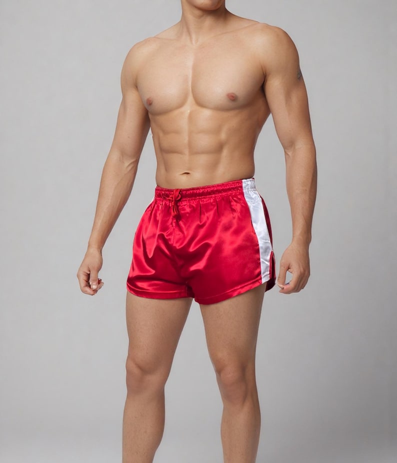 May include: Red satin athletic shorts with a white stripe down the side. The shorts have a drawstring waist and a shiny finish. These shorts are designed for athletic activities.