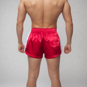 May include: Red satin athletic shorts with white side stripes. The shorts have a classic design with a comfortable fit, suitable for various sports and activities. The shorts feature a back pocket.