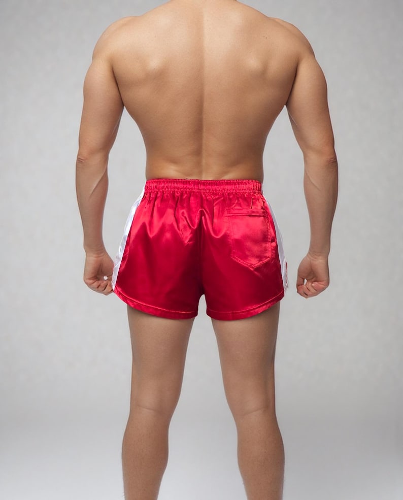 May include: Red satin athletic shorts with white side stripes. The shorts have a classic design with a comfortable fit, suitable for various sports and activities. The shorts feature a back pocket.