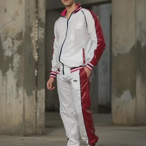 Könnte beinhalten: Weißer und weinroter Trainingsanzug. Die Jacke hat einen weinroten Kragen und Besatz mit einem marineblauen Streifen. Die Hose hat einen weinroten Streifen an der Seite. Das Outfit wird mit weißen Turnschuhen abgerundet.