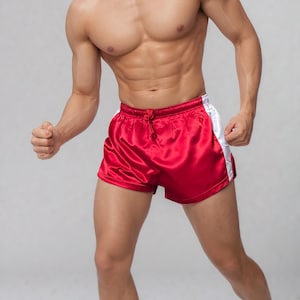 May include: Red satin athletic shorts with white side stripes. The shorts have a drawstring waist and a shiny finish. The shorts are designed for athletic activities and are a vibrant red color.