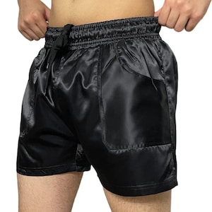 May include: Black satin shorts with a single pocket on the right side. The shorts have a drawstring waistband.