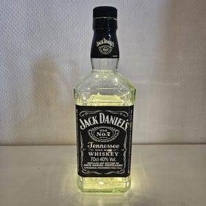Może przedstawiać: Przezroczysta szklana butelka z czarną etykietą, na której widnieje napis "Jack Daniel's Old No.7 Brand Tennessee Sour Mash Whiskey 70cl 40% Vol. Distilled and Bottled by Jack Daniel Distillery Lynchburg, Tennessee 37358 U.S.A."
