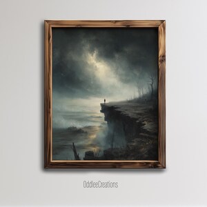 May include: A framed landscape painting depicts a solitary figure on a cliff overlooking a stormy sea. The artwork features a dark, dramatic sky with a hint of light, and a rugged, rocky cliff edge. The frame is made of wood, and the artist's name is visible.