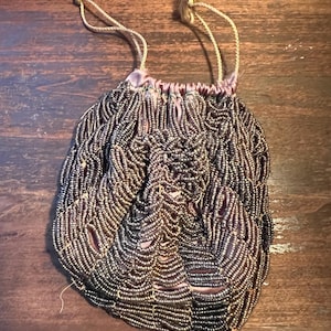 May include: A small, beaded purse with a drawstring closure. The purse is made of dark purple beads and has a satin lining. The purse has two long, gold cords for carrying.