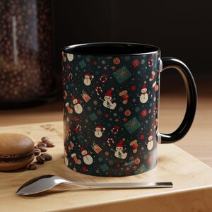 May include: Black ceramic mug with a Christmas-themed design featuring snowmen, candy canes, and gift boxes on a dark blue background.