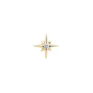 Peut inclure: Boucle d'oreille en forme d'étoile dorée avec une petite pierre précieuse ronde et transparente au centre. La boucle d'oreille a quatre rayons pointus s'étendant vers l'extérieur. Le fond est blanc.