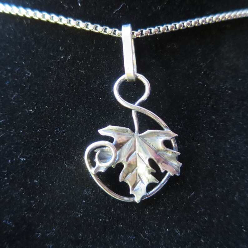 Peut inclure: Un collier avec un pendentif en argent repr&eacute;sentant une feuille d&eacute;taill&eacute;e avec une tige enroul&eacute;e. Le pendentif est attach&eacute; &agrave; une cha&icirc;ne en argent.