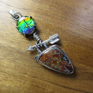 May include: A silver pendant with a teardrop-shaped opal stone and a round opal stone. The pendant features a silver arrow design.