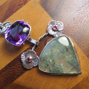 May include: A silver pendant necklace with a large, faceted amethyst gemstone, two smaller pink gemstones, and a triangular green stone.