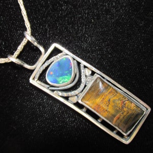 May include: A silver pendant necklace with a rectangular frame featuring a blue opal and a tiger's eye stone.
