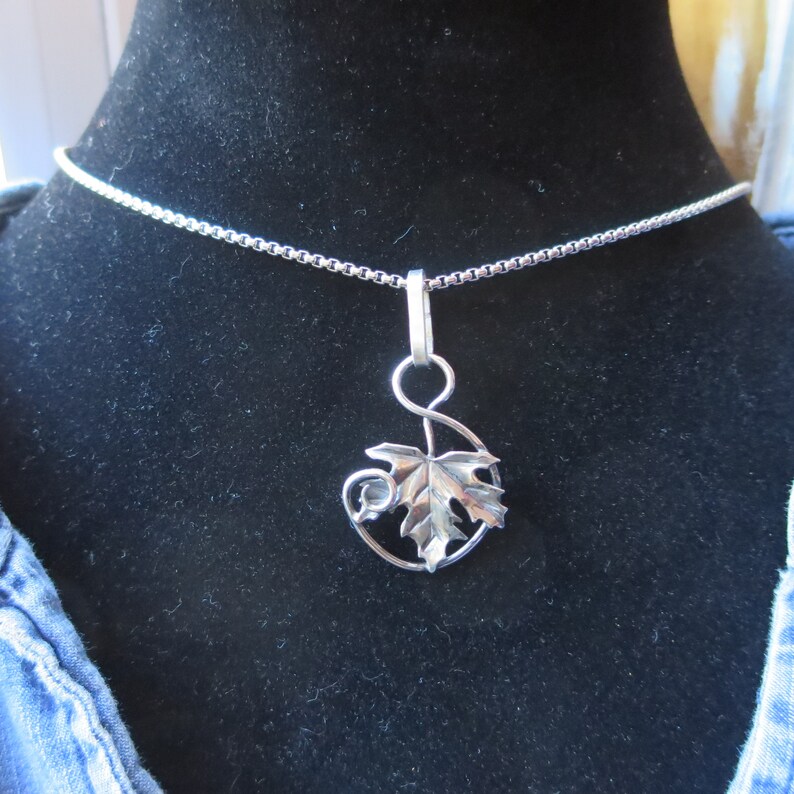 Peut inclure: Un collier en argent avec une cha&icirc;ne d&eacute;licate et un pendentif en forme de feuille avec une vigne.