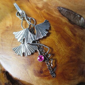 May include: A silver pendant featuring three ginkgo leaves with a pink gemstone hanging from a chain.