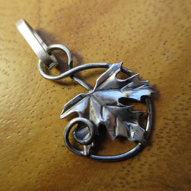 Peut inclure: Un pendentif en argent avec un motif de feuille d&eacute;taill&eacute; et une vigne enroul&eacute;e. Le pendentif est attach&eacute; &agrave; une cha&icirc;ne en argent.