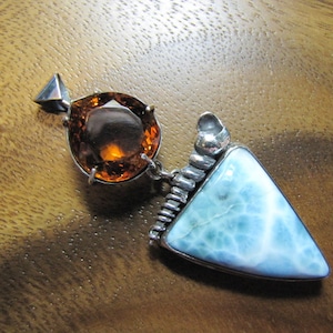 May include: A silver pendant with a triangular blue and white gemstone and a round orange gemstone.