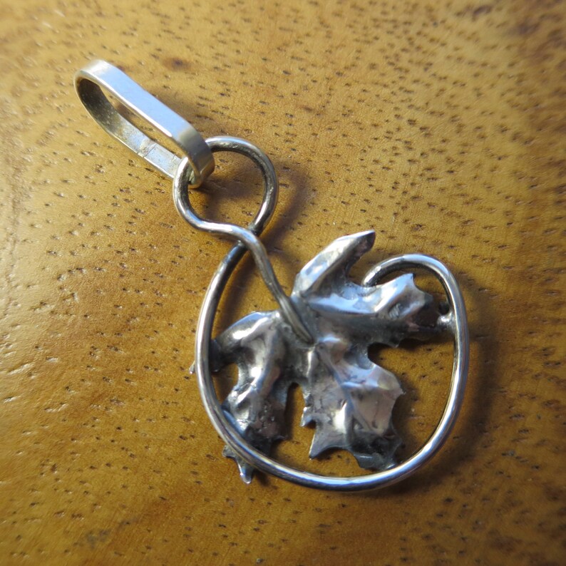 Peut inclure: Un pendentif en argent avec un motif de feuille d'&eacute;rable textur&eacute; et d&eacute;taill&eacute;, une tige de vigne torsad&eacute;e et une boucle pour attacher une cha&icirc;ne.