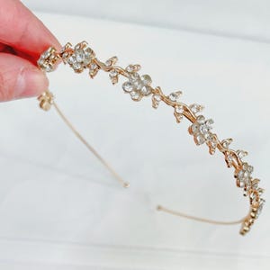 May include: A gold headband with a delicate floral design featuring small, clear rhinestones. The headband is thin and flexible, making it comfortable to wear.