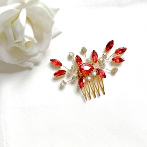 May include: A gold hair comb with a red and clear crystal design. The comb has a floral shape with a large red crystal in the center.
