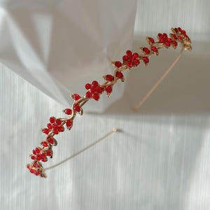 May include: A gold headband with a vine design adorned with red rhinestones. The headband is a simple and elegant accessory for any occasion.