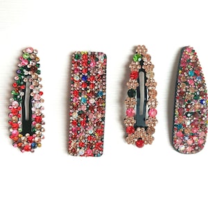 Peut inclure: Quatre pinces à cheveux avec une variété de strass colorés. Les pinces sont noires et ont une forme rectangulaire ou ovale.