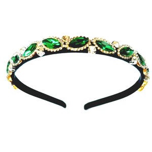 May include: A black headband decorated with emerald green and clear crystal gemstones. The gemstones are set in gold-coloured metal, creating a sparkling and elegant accessory. The headband is a stylish hair accessory.