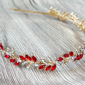 May include: Gold headband with a delicate design of red and clear rhinestones arranged in a leaf pattern.