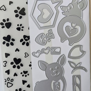 May include: A Sizzix Thinlits die set with textured impressions. The set includes a clear stamp with paw prints and hearts, and metal dies of a corgi dog, hearts, and other shapes. The packaging includes the names Katelyn Lizardi and Lindsey Serata.
