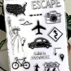 May include: A set of 16 clear photopolymer stamps titled World Traveler featuring black ink designs of the United States map, the Statue of Liberty, a camera, an airplane, a car, a bicycle, a Route 66 sign, and text including ESCAPE and ticket to ANYWHERE.