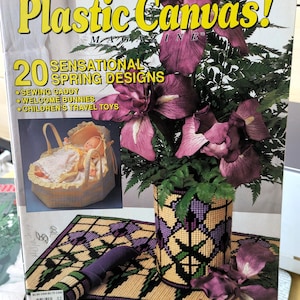May include: A magazine cover titled "Plastic Canvas!" with the text "20 Sensational Spring Designs." The cover features a doll in a basket, a vase with purple flowers, and a matching placemat. The magazine also includes sewing caddy, welcome bunnies, and children's travel toys.