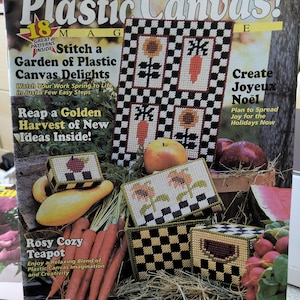 May include: A magazine cover titled "Plastic Canvas!" features cross-stitch projects with a garden theme. The cover includes text such as "Stitch a Garden of Plastic Canvas Delights" and images of stitched sunflowers, carrots, and boxes.