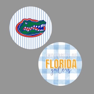 May include: Two circular stickers. The top sticker features a green alligator head logo with orange and blue outlines on a light blue and white vertical striped background. The bottom sticker displays the text University of Florida Gators on a light blue gingham pattern.