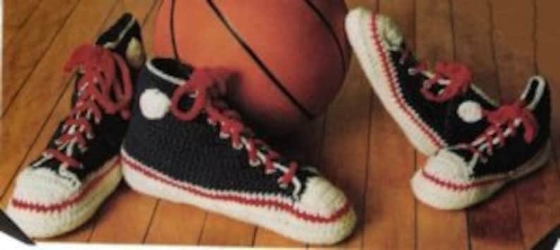 May include: Handmade crochet high-top sneakers in navy blue, white, and red. The sneakers feature white toe caps, red laces, and a white circle on the side. A basketball is in the background.