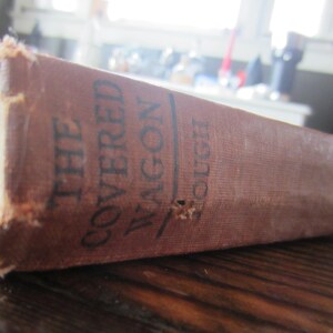 Puede incluir: Un libro antiguo de tapa dura titulado "The Covered Wagon" de Emerson Hough.