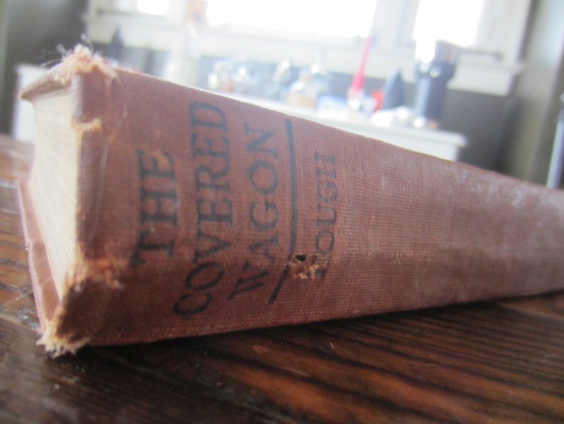 Puede incluir: Un libro antiguo de tapa dura titulado "The Covered Wagon" de Emerson Hough.