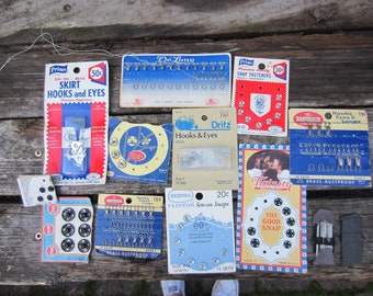 May include: Assortment of vintage sewing notions, including hooks and eyes, snap fasteners, sew-on snaps, and buttons. The packaging is colorful and features various brands, including Prims, Dritz, and Clinton.