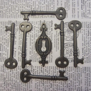 May include: A collection of ten antique-style skeleton keys in a silver finish. The keys are arranged on a page of a book with text.  The keys are various sizes and shapes, with some featuring intricate designs.