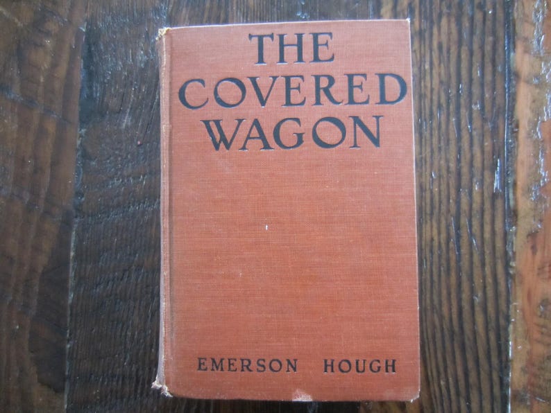 Puede incluir: Un libro vintage titulado "The Covered Wagon" de Emerson Hough. El libro tiene una cubierta roja con texto negro.