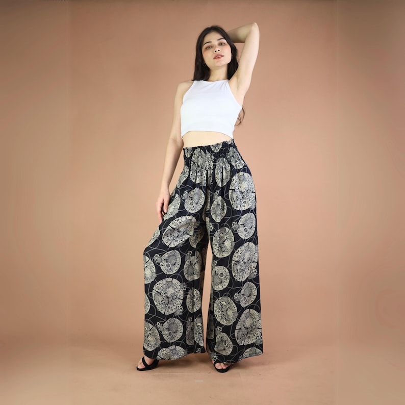 May include: Black wide-leg pants with a white and gold floral print. The pants have an elastic waistband and a relaxed fit.