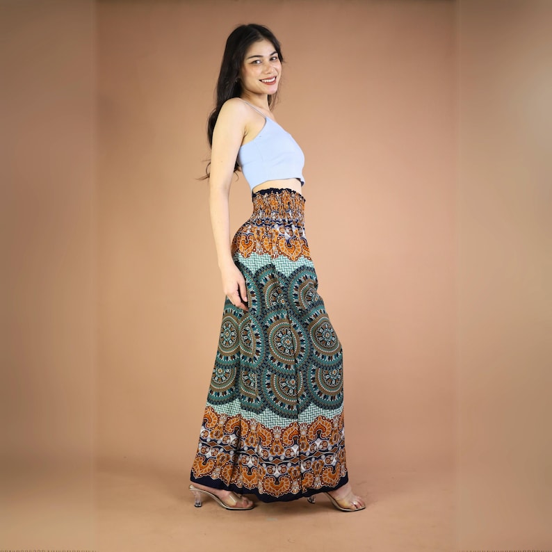 May include: A woman wearing a light blue tank top and a long, flowing skirt with a colorful mandala pattern. The skirt has a high waist and a wide elastic waistband. The skirt is made of a soft, lightweight fabric.