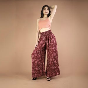 May include: A woman wearing a pink tank top and wide-legged pants with a floral print. The pants have an elastic waistband and a loose, flowing fit.