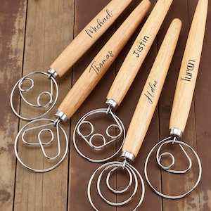 Peut inclure: Cinq fouets en bois personnalisés avec des boucles en fil d'acier inoxydable. Chaque manche est gravé d'un nom : Michael, Thomas, Jistin, Helen et Turan. Les fouets sont disposés sur une surface en bois.