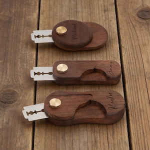 Peut inclure: Trois rasoirs droits personnalisés en bois avec lames apparentes et accents en laiton. Chaque rasoir est gravé d'un nom : Michael, Jimmy et Kristie. Les rasoirs sont présentés sur une surface en bois.