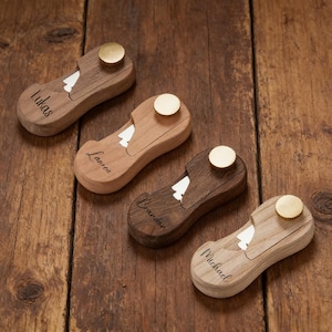 May include: Four wooden bottle openers with brass tops and personalized names: Lukas, Lauren, Brandon, and Michael. Each opener has a tree-shaped cutout and a natural wood finish, varying in shades from light to dark brown.