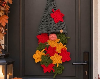 May include: A hanging crochet gnome decoration featuring a tall dark gray pointed hat, a round peach-colored nose, and a long beard constructed from numerous individual crocheted maple leaves in vibrant shades of red, orange, and forest green.