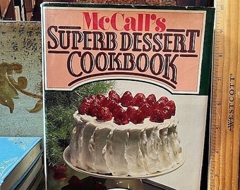 May include: A vintage cookbook titled "McCall's Superb Dessert Cookbook" by Mary Eckley, Food Editor of McCall's. The cover features a white cake with red berries on top, sitting on a cake stand.
