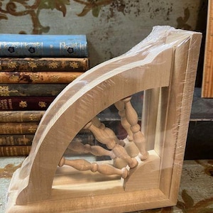 May include: A wooden shelf bracket with a decorative cutout design featuring a half-circle with a series of wooden dowels arranged in a radial pattern. The bracket is made of light-colored wood and has a natural finish.