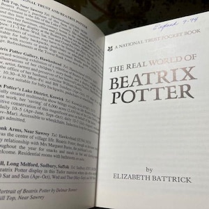 May include: Open book titled "The Real World of Beatrix Potter" by Elizabeth Battrick. The cover is white with silver lettering. The left page contains text about Beatrix Potter's life and locations.